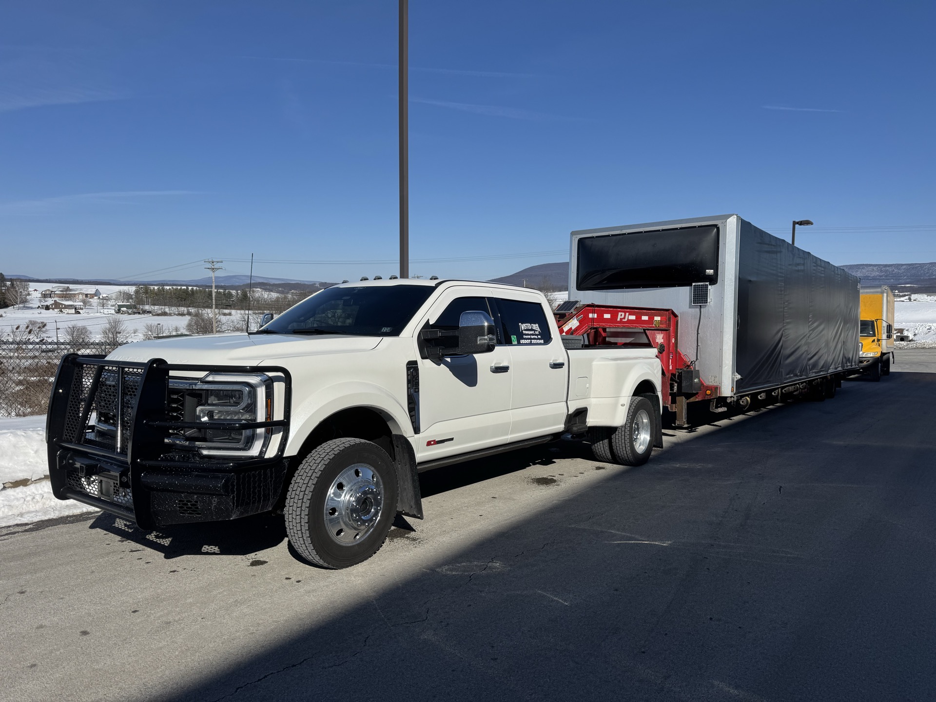 White Ford pickup with a covered gooseneck load parked in a snowy lot