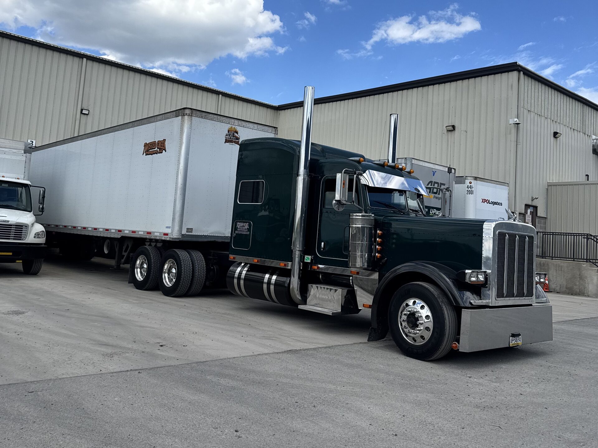 Green Peterbilt with a dry van trailer parked alongside a warehouse building